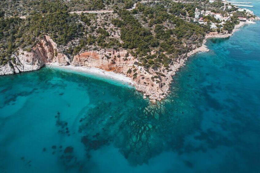 An aerial view of a coastal area with a sandy beach, clear turquoise waters, and a rocky coastline. 4