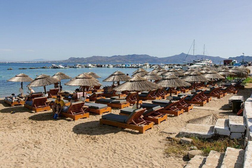 A beach with rows of sun loungers and thatched umbrellas, a clear sky, and boats in the background. 3