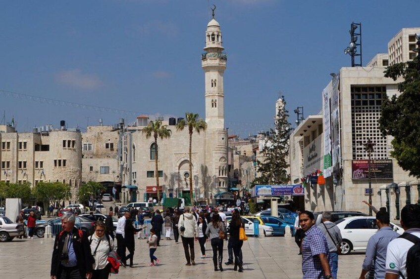 A busy urban square with a prominent mosque, pedestrians, and commercial buildings. 2
