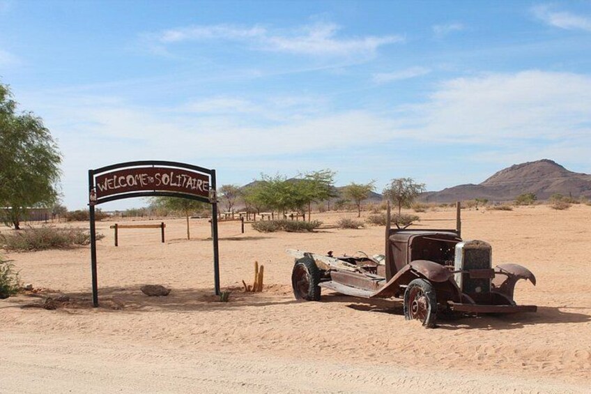 A vintage car parked in a desert with a sign that reads 'Welcome to Solitude.' 2