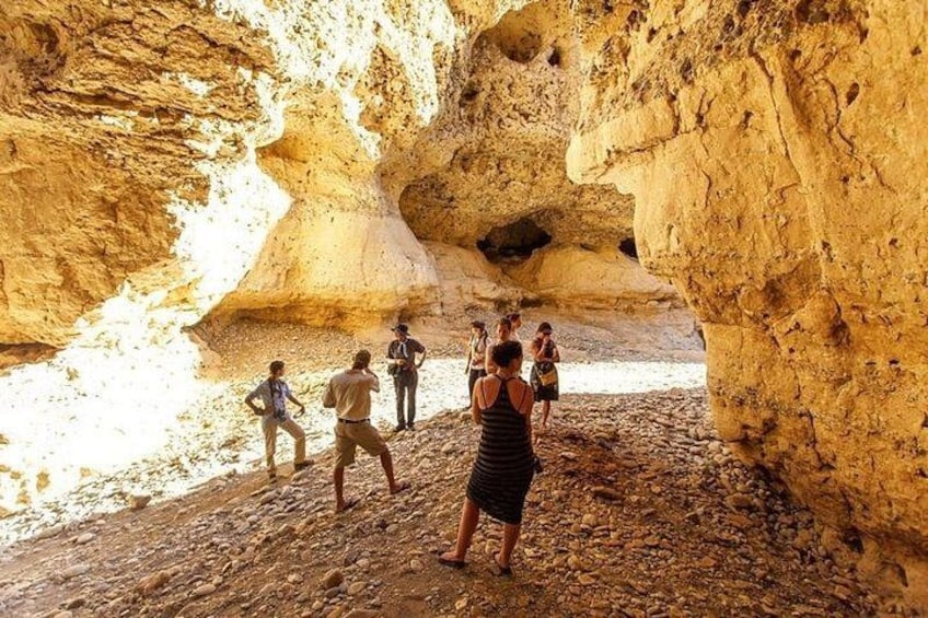 A group of people exploring a rocky cave with a large opening. 5