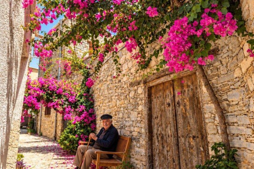 Een man zit op een bankje in een smalle straat met stenen muren en felroze bougainvilleablaadjes. 4