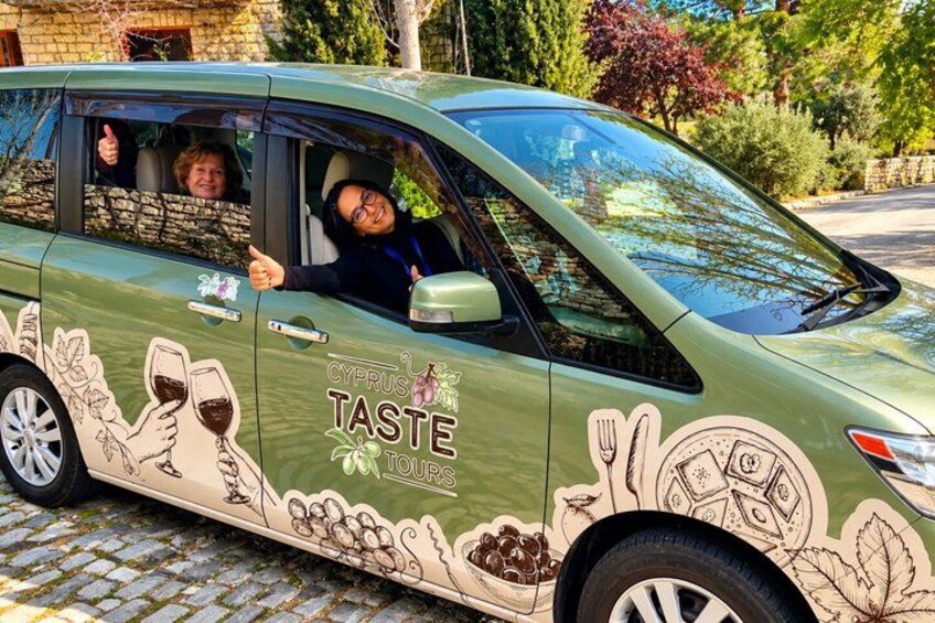 Een groene auto met een 'CYPRUS TASTE TOUR' sticker, geparkeerd op een geplaveid straat. 2