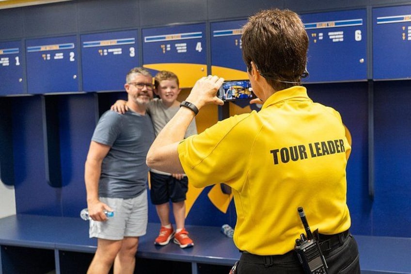 Un guide accompagnateur, vêtu d’un maillot jaune avec l’inscription « GUIDE » dans le dos, échange avec deux enfants dans un vestiaire. 4
