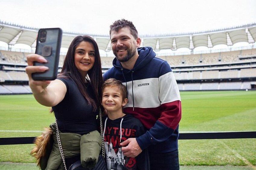 A family taking a selfie in a stadium with a green field and empty stands. 3