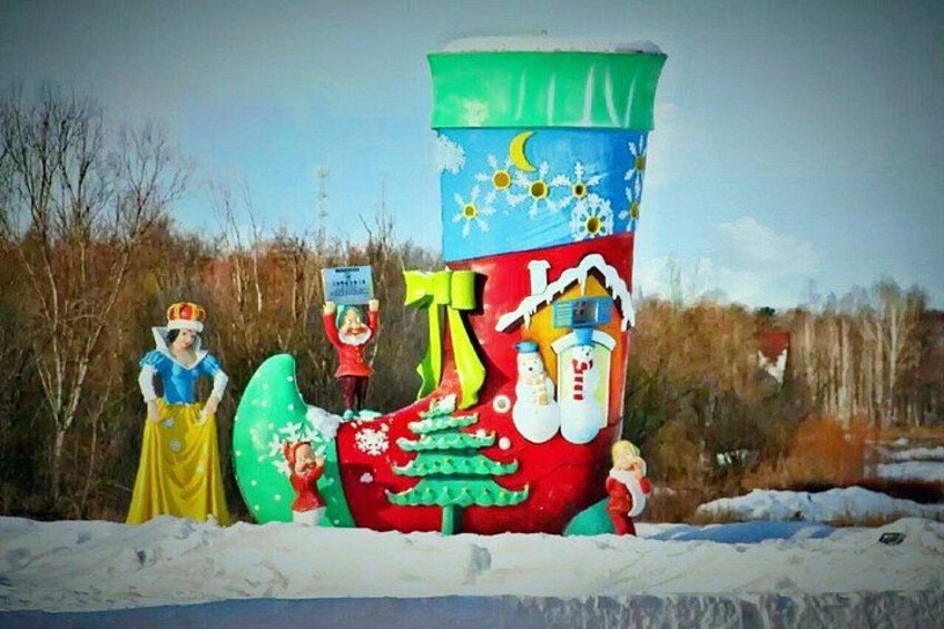 A large snowman sculpture with a Christmas tree and a crown, set in a snowy landscape with bare trees and a clear sky. 3