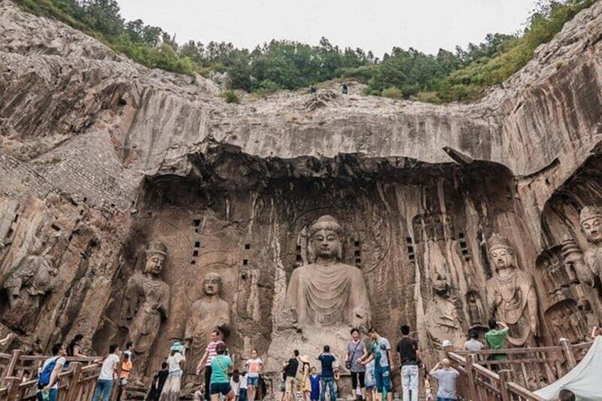 En stor klippformation med flera Buddha-statyer som är huggna in i den, omgiven av besökare. 1
