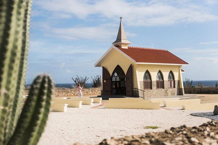 En liten kyrka med ett rött tak och ett torn, omgiven av ökenväxter och en klar himmel. 4
