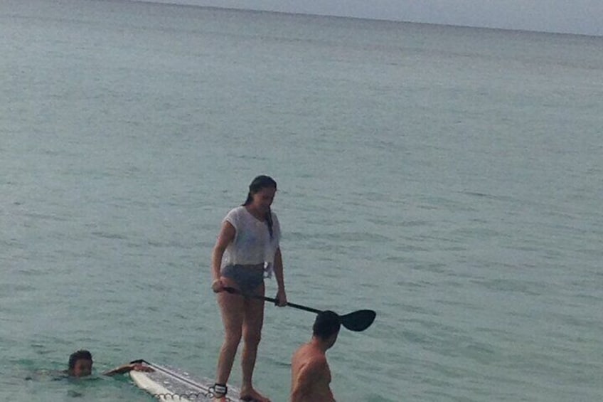 Una persona de pie sobre una tabla de surf en el agua, otra persona remando cerca y una tercera persona nadando. 5