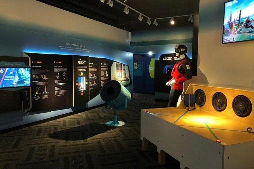 En udstilling indendørs med en VR-flysimulator, informationstavler og en stor model af et fly. 5
