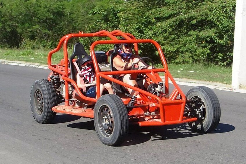 A red go-kart on a paved road with greenery in the background. 2