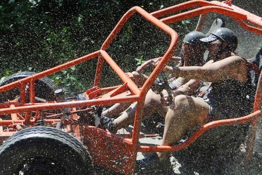 A person in a red vehicle with a large tire, driving through a water spray. 3
