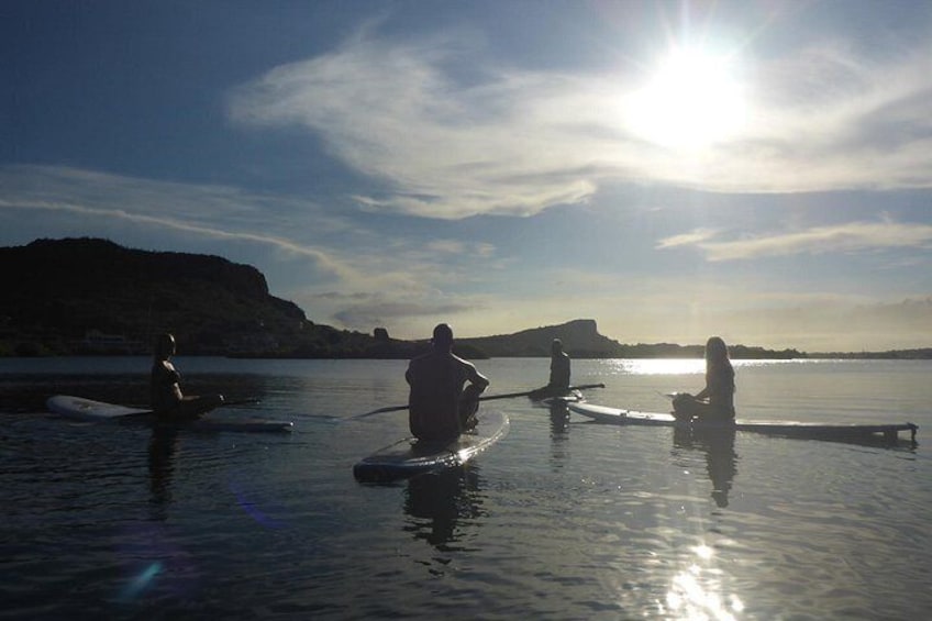 Personas remando en tablas de surf sobre aguas tranquilas, con cielo despejado y accidentes geográficos lejanos. 4