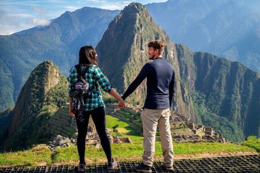 Two people holding hands, overlooking Machu Picchu ruins with steep mountains in the background. 4