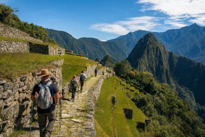 A stone pathway with hikers, surrounded by lush green hills and mountains. 1