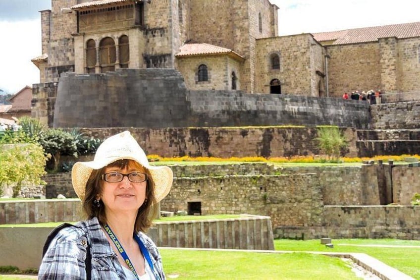 Una persona con cappello e camicia a quadri in piedi di fronte a un edificio storico in pietra con un muro fortificato. 4