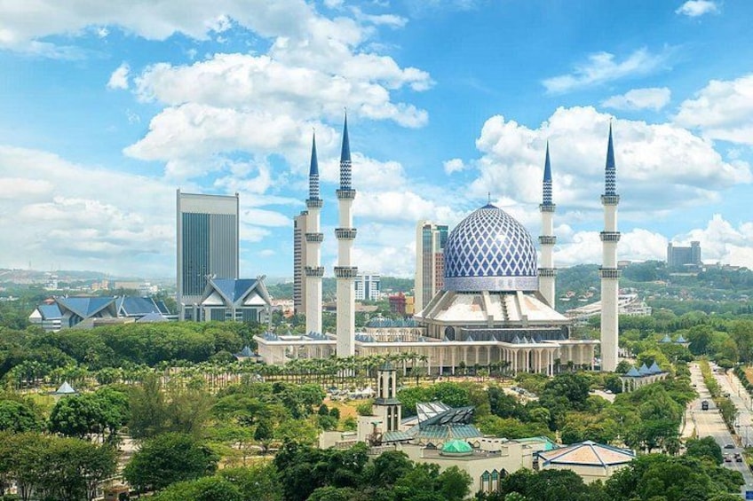 A mosque with a large dome and four minarets, surrounded by greenery and modern buildings. 3