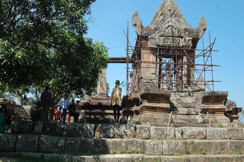A temple under construction with scaffolding, surrounded by stone steps and a large tree. 5