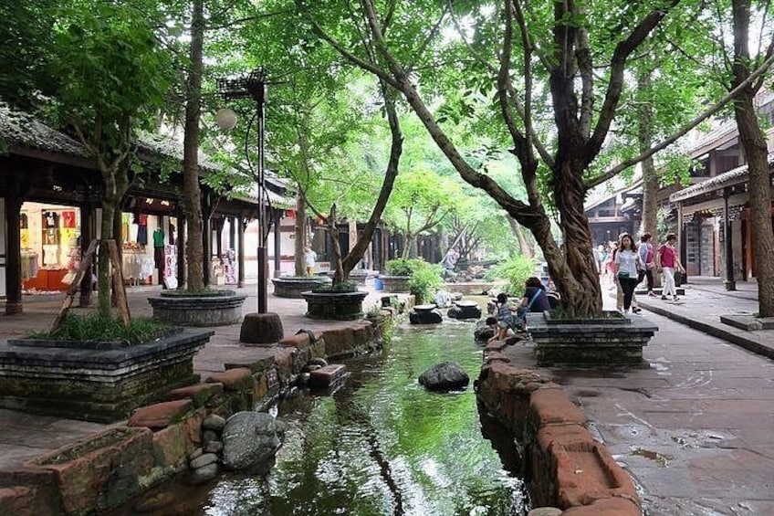 A traditional street with a water channel, stone lanterns, and trees. 2