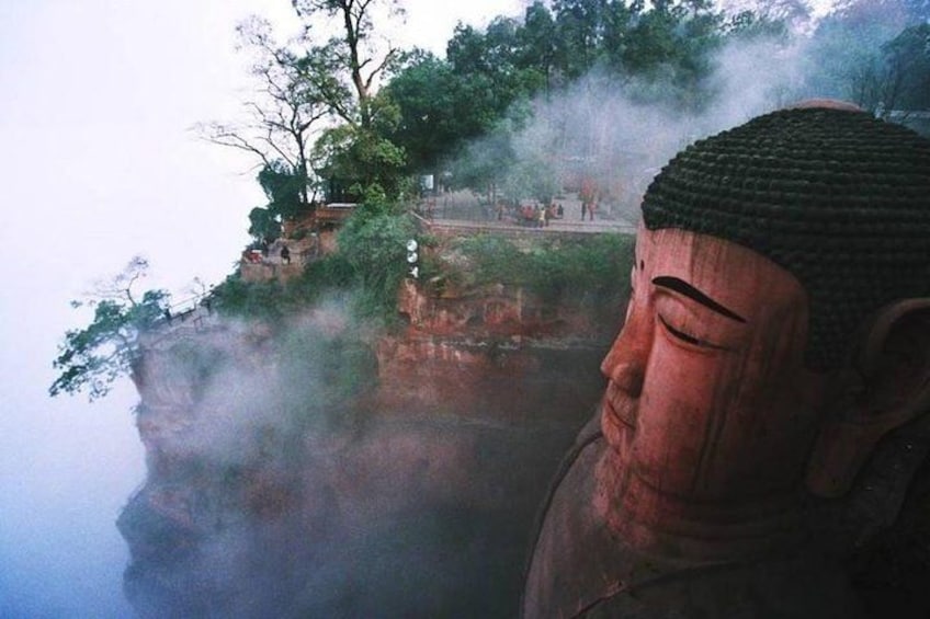 A large Buddha statue on a cliff with a temple in the background. 3