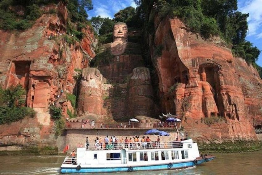 A large rock formation with a statue, a boat with people, and a river. 2
