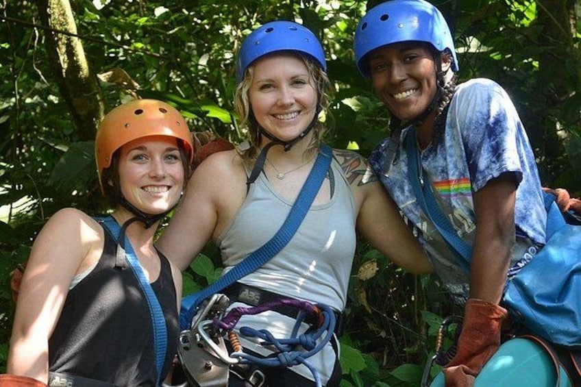 Three people wearing helmets and harnesses, suggesting they are engaged in an outdoor activity, possibly zip-lining or rappelling, in a wooded area. 4
