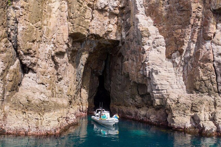 Un bateau navigue à travers l’entrée rocheuse d’une grotte, entourée de falaises. 2