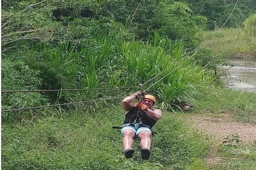 A person sitting on a rope swing in a grassy area with dense vegetation and a dirt path in the background. 1