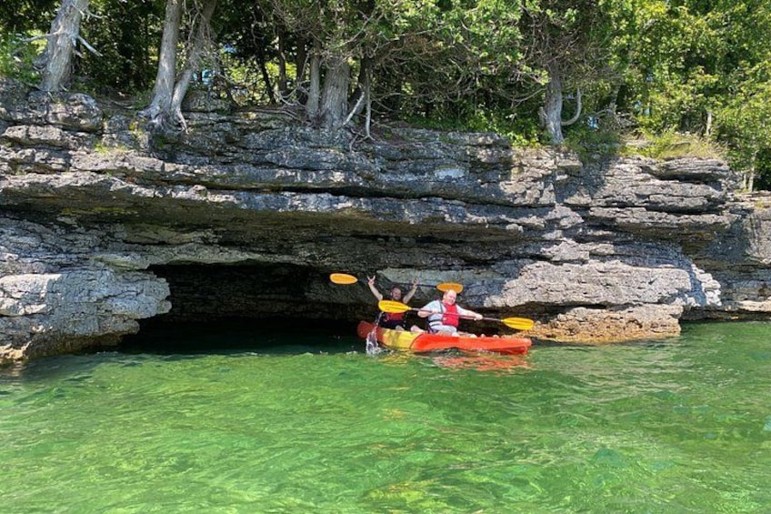 Dos personas haciendo kayak cerca de la entrada de una cueva rocosa. 1