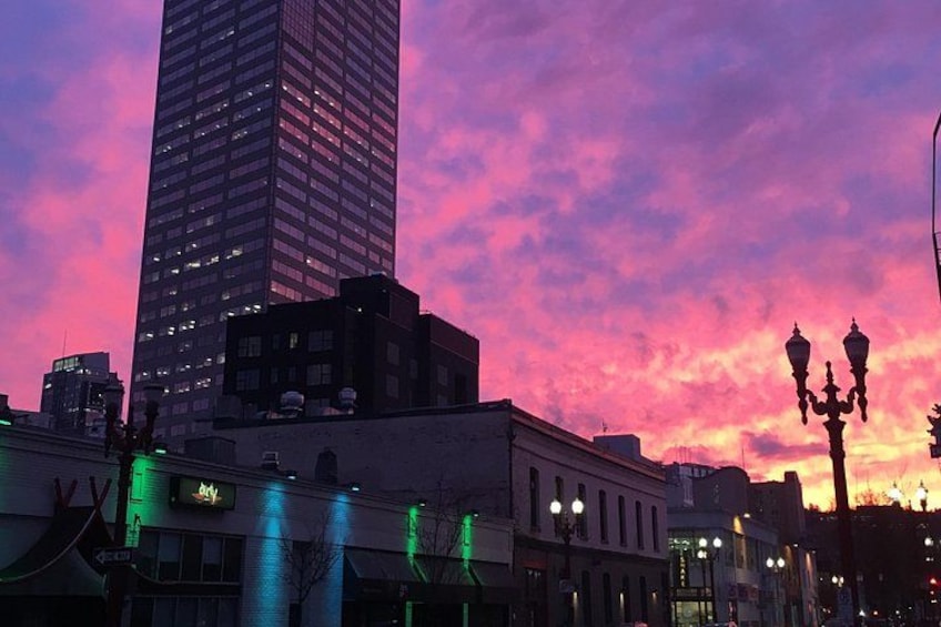A city skyline with a tall building, street lamps, and illuminated buildings against a colorful sky. 1