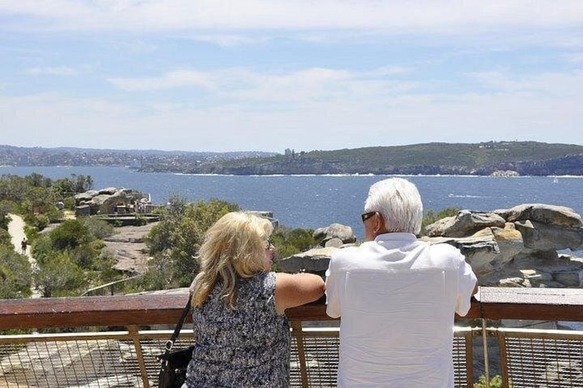 Deux personnes contemplent un paysage côtier caractérisé par un terrain rocheux et, au loin, la silhouette d’une ville. 3