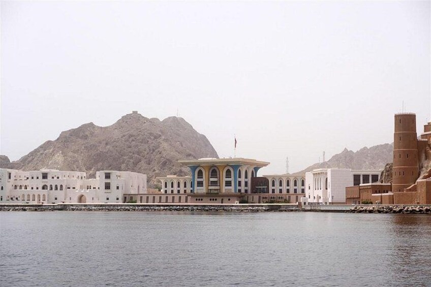 A coastal cityscape with a prominent building with blue arches, a large mountain in the background, and a body of water in the foreground. 3