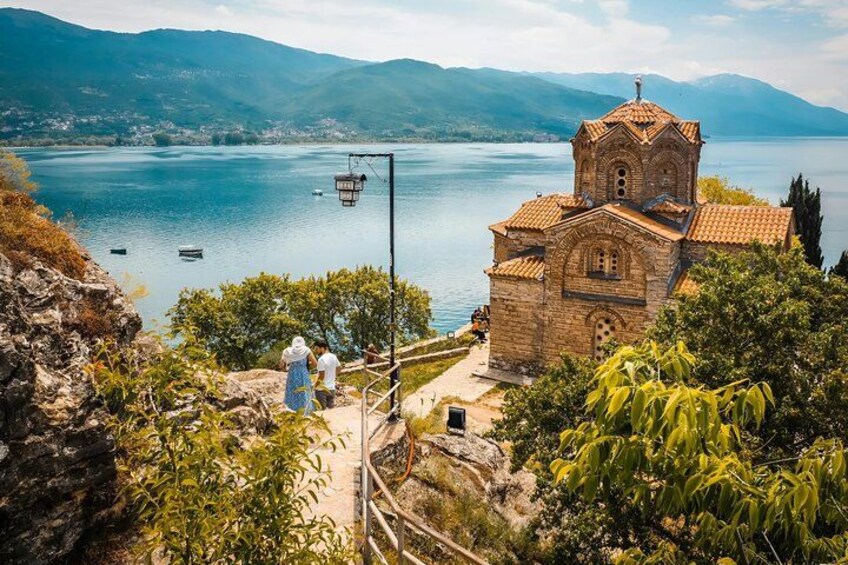 A church with a bell tower, a lake, and mountains in the background. 1