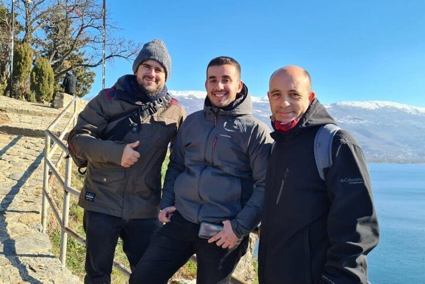 Three people standing on a stone staircase with a lake and mountains in the background. 3
