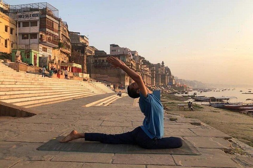 A person performing a yoga pose on a mat by a riverside with buildings in the background. 2