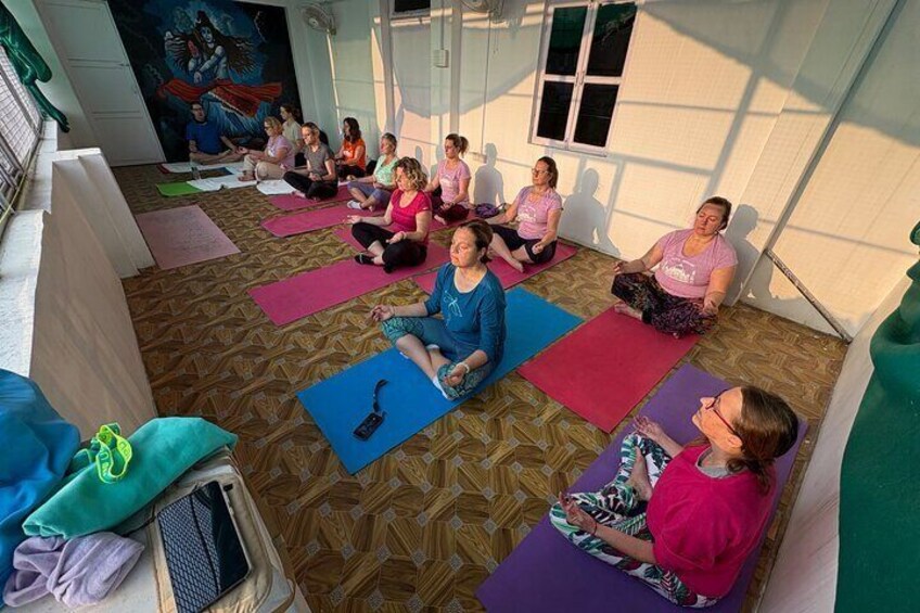 A group of people sitting on yoga mats in a room with patterned flooring and a mural on the wall. 1