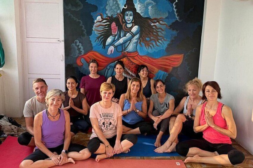 A group of people sitting on mats in a room with a large mural of a figure in a blue robe. 3