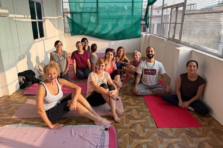 A group of people sitting on yoga mats in a room with a patterned floor and a green netting structure. 2