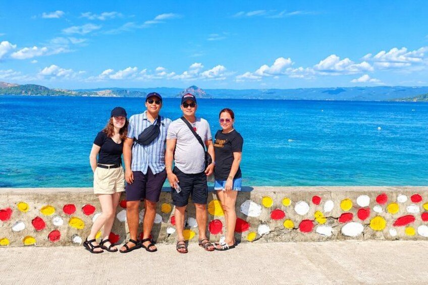 A group of people standing by a colorful wall with a view of the sea and distant hills. 5