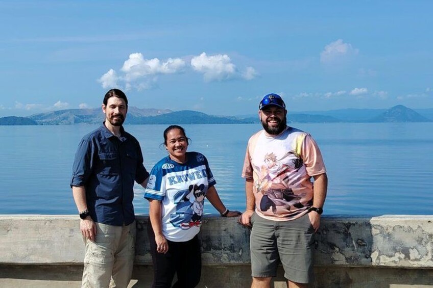 Trois personnes se tiennent au bord de l’eau, sous un ciel dégagé, avec des montagnes qui se dessinent à l’horizon. 5