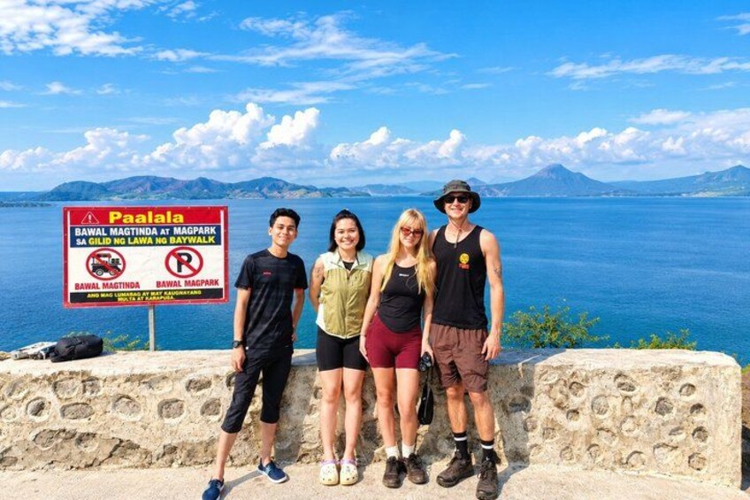 A group of people standing by a sign with a scenic view of a bay and mountains in the background. 4