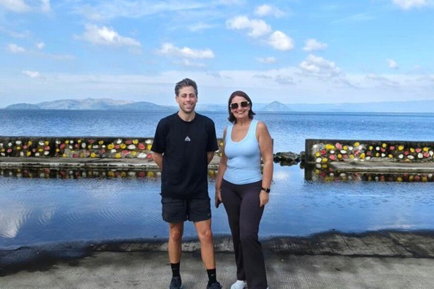 Deux personnes se tiennent sur un quai, avec une étendue d’eau et des montagnes en arrière-plan. 4