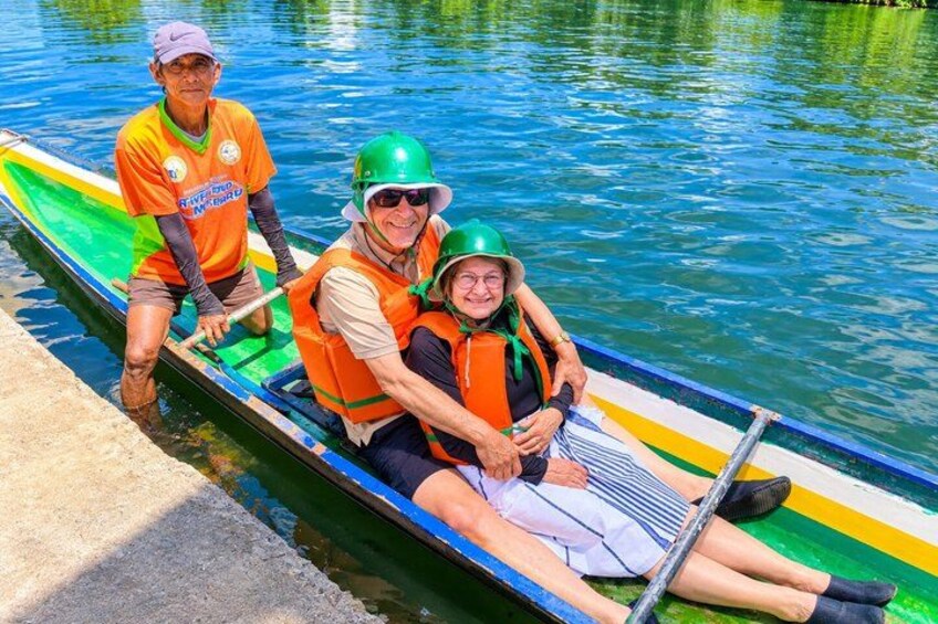 Three people in a rowboat wearing life jackets and helmets, paddling on a calm body of water. 2