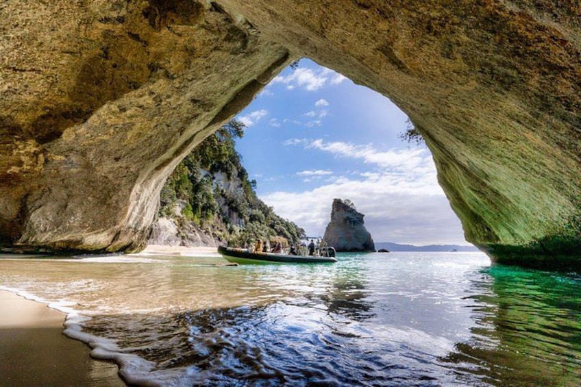 A boat under a natural rock arch, clear water, and a distant rocky island. 5