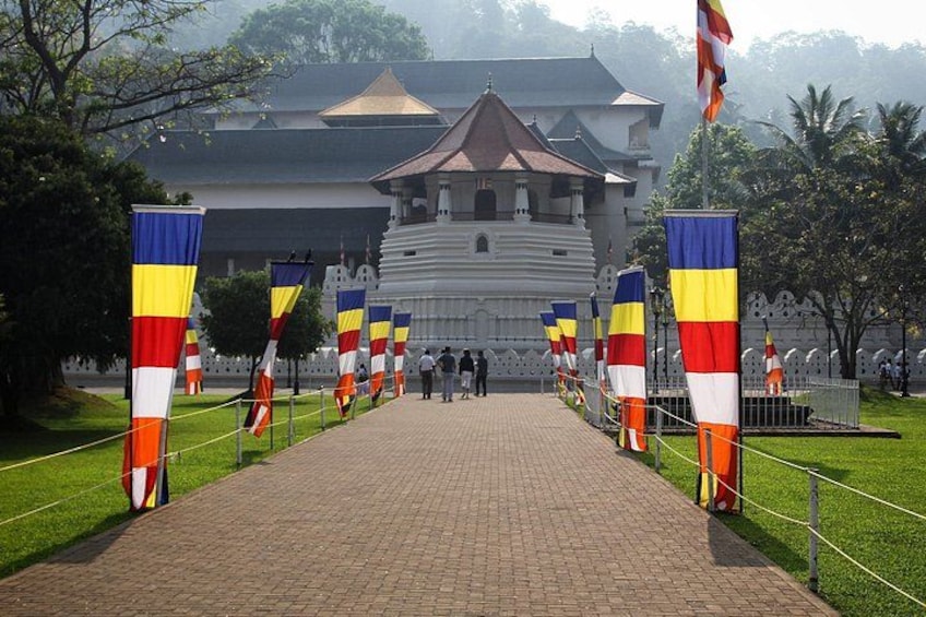 A pathway leading to a white building with a traditional roof, flanked by flags. 5