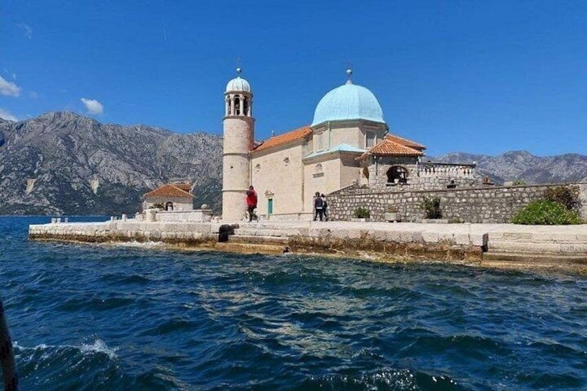 A coastal church with a blue dome and bell tower, surrounded by water and mountains. 4