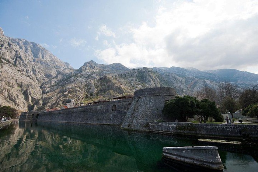 A historic stone fortress by a calm lake with mountains in the background. 5