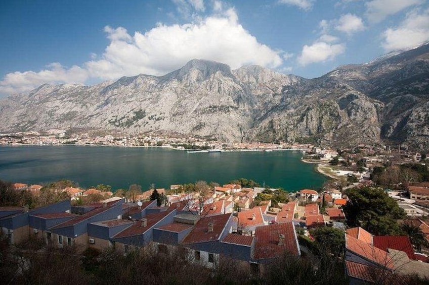 A coastal town with red-roofed buildings, a large body of water, and mountains in the background. 5