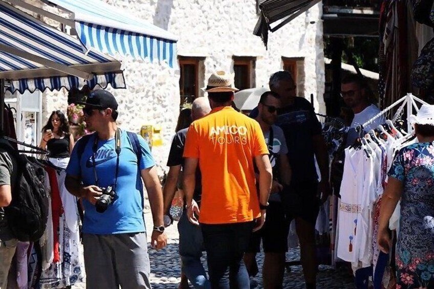 A street market with people walking, a man in an orange shirt, and a man with a camera. 5