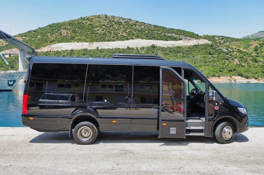 A black van parked by a body of water with a hilly landscape in the background. 2
